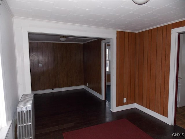 unfurnished room with dark wood-style floors, baseboards, wood walls, and radiator heating unit