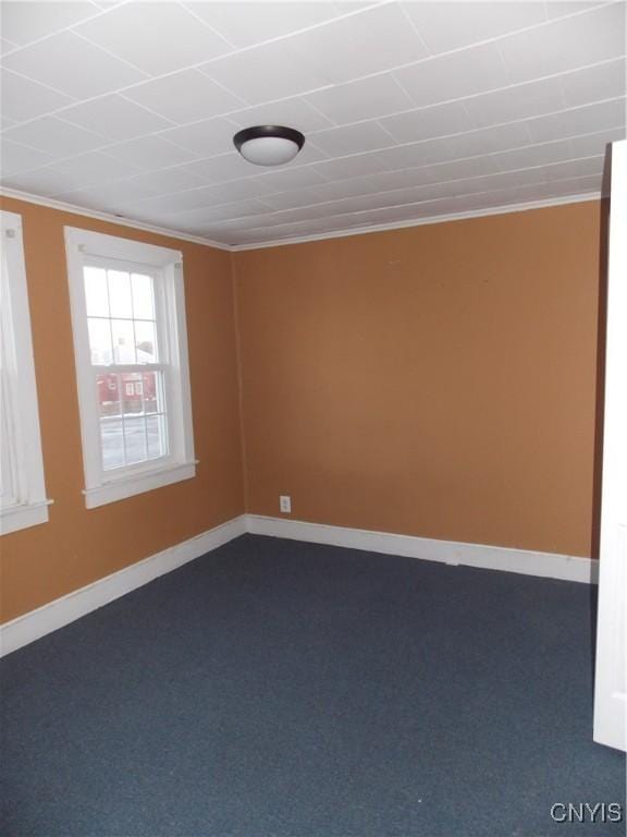 empty room with baseboards, dark carpet, and ornamental molding