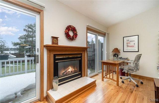 office area with lofted ceiling, a tiled fireplace, wood finished floors, and baseboards