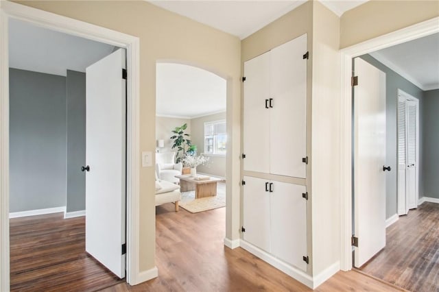 hall featuring arched walkways, wood finished floors, and baseboards