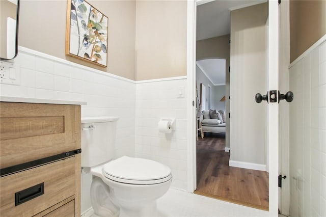 bathroom with wainscoting, wood finished floors, toilet, and tile walls