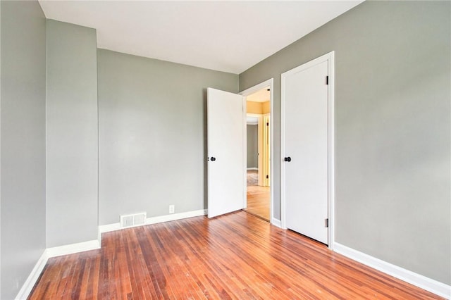 spare room with baseboards, visible vents, and wood finished floors