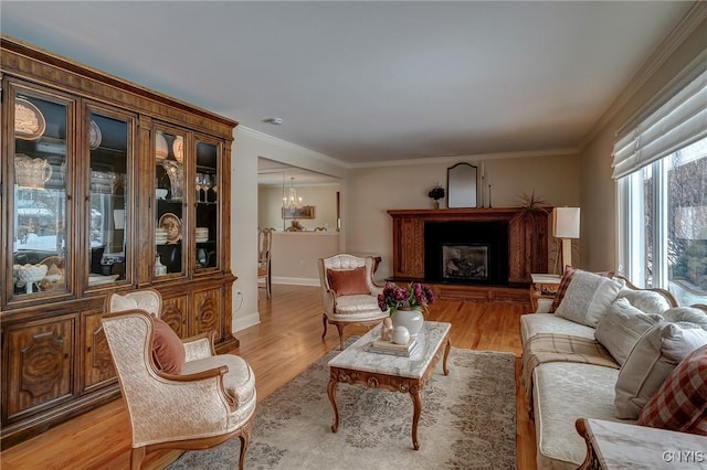 living room featuring crown molding, baseboards, light wood-type flooring, a glass covered fireplace, and an inviting chandelier