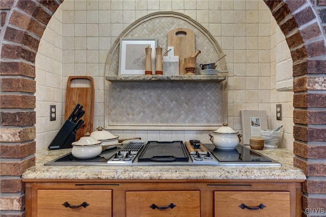 kitchen featuring stovetop with downdraft, backsplash, and brown cabinets