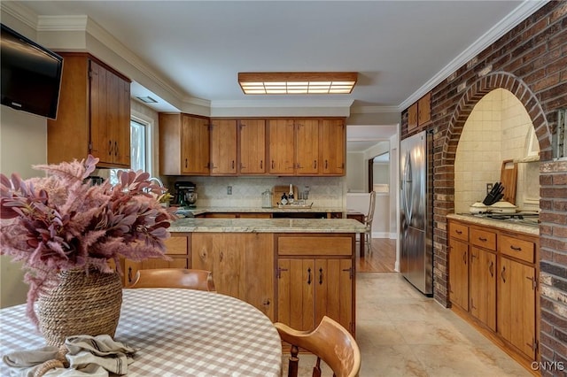 kitchen featuring stainless steel fridge, decorative backsplash, brick wall, brown cabinets, and a sink