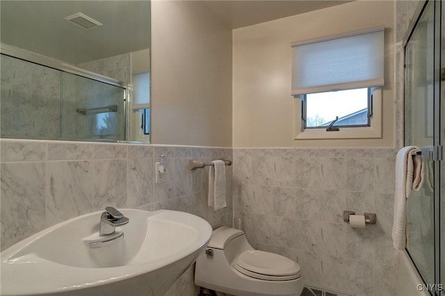 full bathroom with visible vents, toilet, a sink, a shower stall, and tile walls