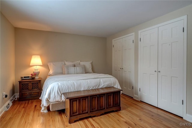 bedroom with light wood-type flooring, baseboards, visible vents, and multiple closets