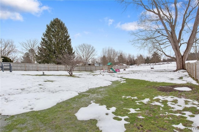 yard layered in snow with a playground and a fenced backyard