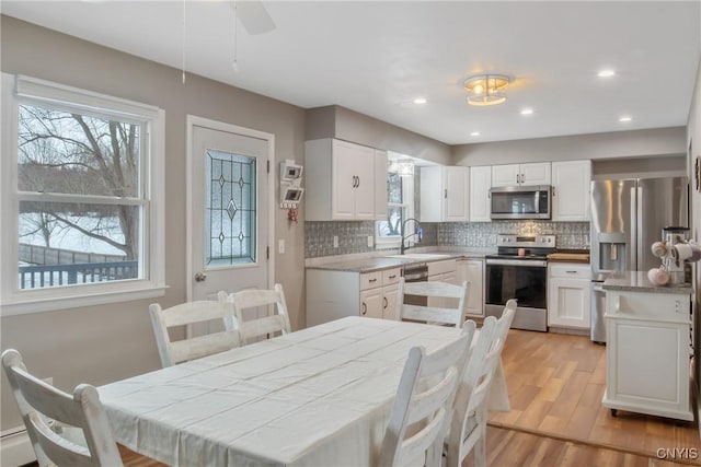 kitchen with light wood-style flooring, stainless steel appliances, a sink, white cabinetry, and decorative backsplash