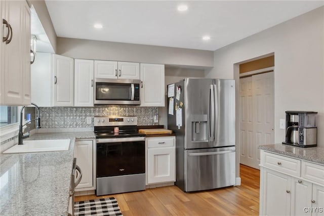 kitchen with stainless steel appliances, a sink, white cabinetry, light wood-style floors, and decorative backsplash