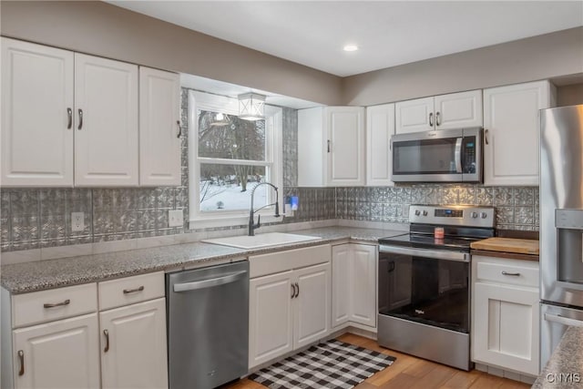 kitchen with stainless steel appliances, tasteful backsplash, a sink, and white cabinetry