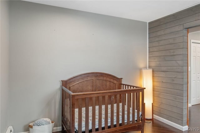 bedroom featuring wooden walls, wood finished floors, baseboards, baseboard heating, and a crib