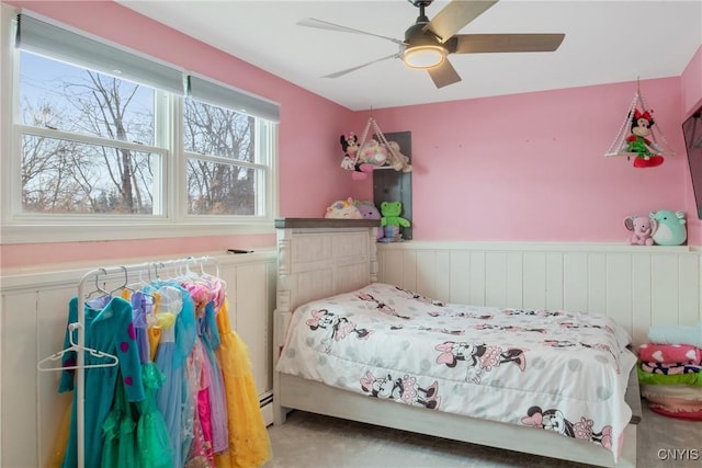 bedroom featuring a wainscoted wall, baseboard heating, and a ceiling fan