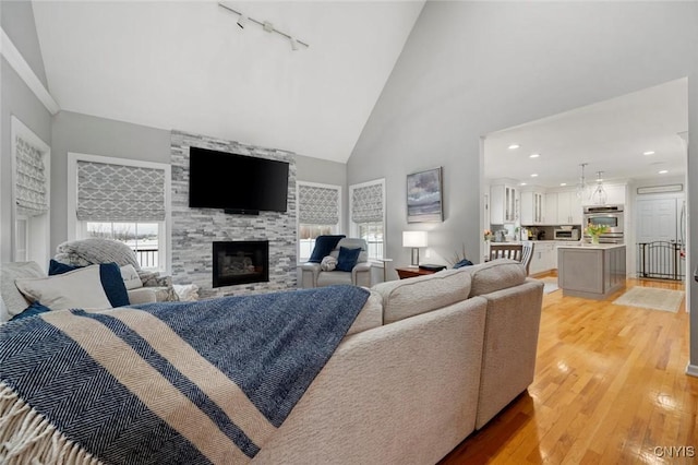 living area with high vaulted ceiling, light wood-type flooring, a fireplace, and plenty of natural light