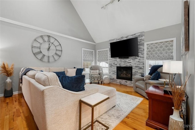 living area featuring light wood-style floors, a large fireplace, track lighting, high vaulted ceiling, and baseboards