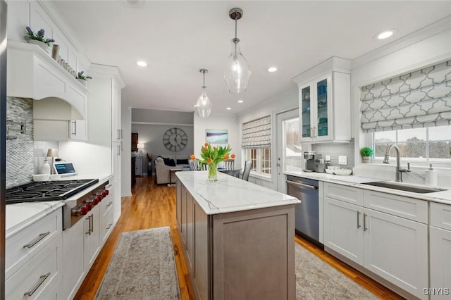 kitchen with light wood-style flooring, a center island, stainless steel appliances, white cabinetry, and a sink