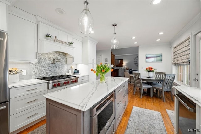 kitchen with stainless steel appliances, white cabinetry, decorative backsplash, a center island, and light wood finished floors