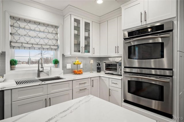 kitchen with a sink, glass insert cabinets, decorative backsplash, and stainless steel double oven