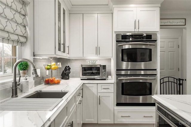 kitchen featuring stainless steel double oven, a toaster, a sink, white cabinets, and tasteful backsplash