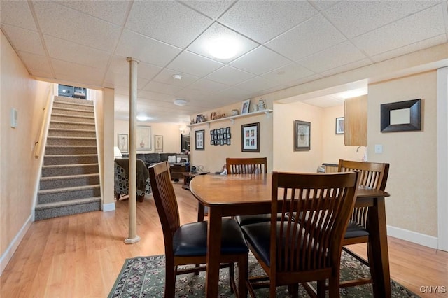 dining space with baseboards, stairway, a drop ceiling, and light wood-style floors