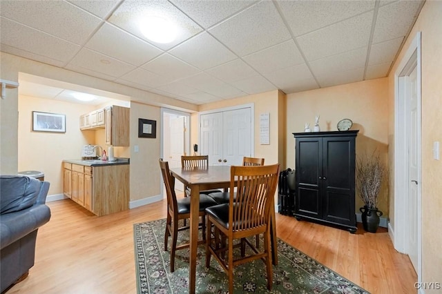 dining space with light wood-type flooring, baseboards, and a drop ceiling