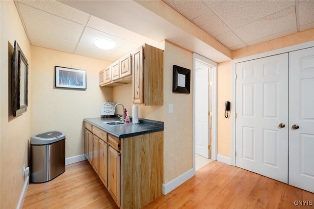 kitchen with light wood finished floors, dark countertops, a sink, and a paneled ceiling