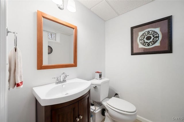 half bathroom with a paneled ceiling, toilet, and vanity