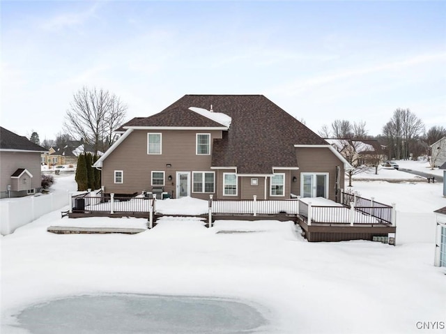 snow covered rear of property with a shingled roof and a wooden deck