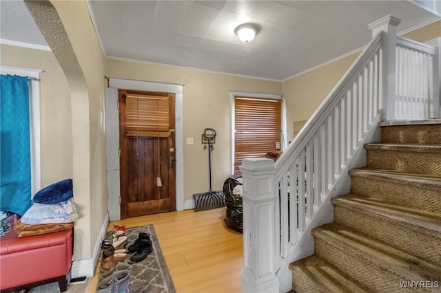 foyer entrance with arched walkways, light wood-style flooring, baseboards, stairway, and crown molding