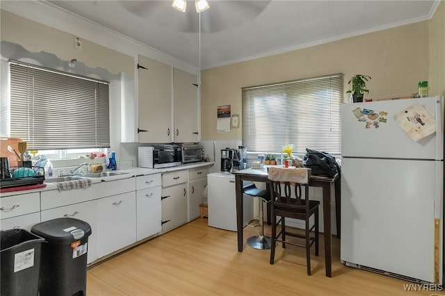 kitchen featuring light wood-style flooring, white cabinets, freestanding refrigerator, stainless steel microwave, and crown molding