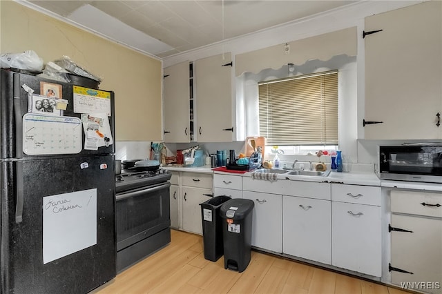 kitchen with light wood finished floors, stainless steel appliances, light countertops, white cabinetry, and a sink