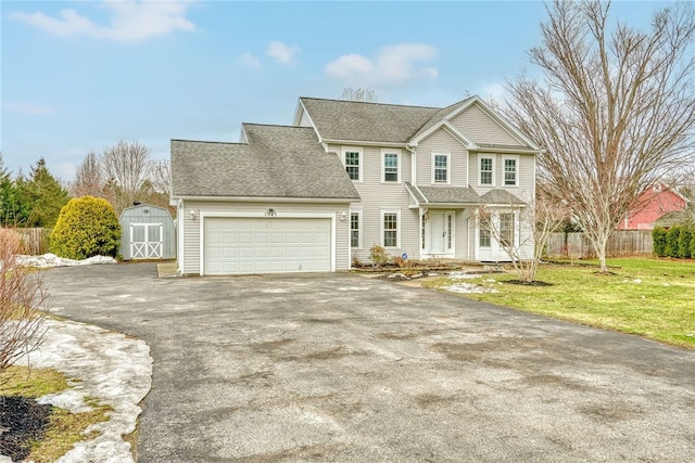 view of front of house featuring an attached garage, fence, a shed, driveway, and a front lawn