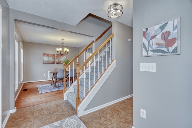 staircase with a notable chandelier, baseboards, and tile patterned floors