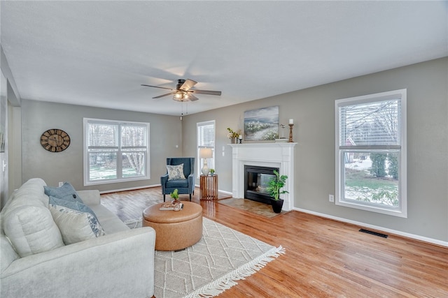 living room featuring a fireplace with flush hearth, light wood-type flooring, visible vents, and plenty of natural light