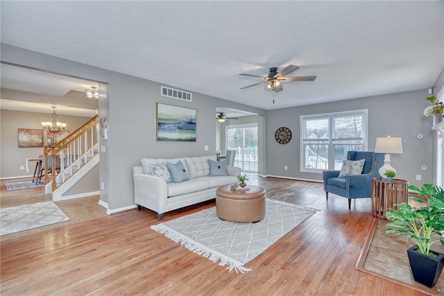 living area with ceiling fan with notable chandelier, wood finished floors, visible vents, baseboards, and stairs