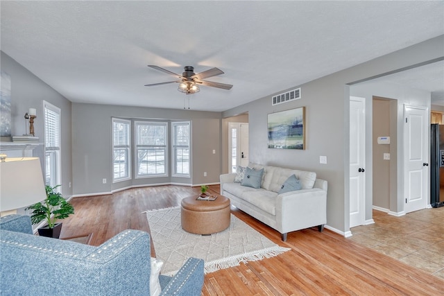 living area featuring baseboards, a ceiling fan, visible vents, and light wood-style floors