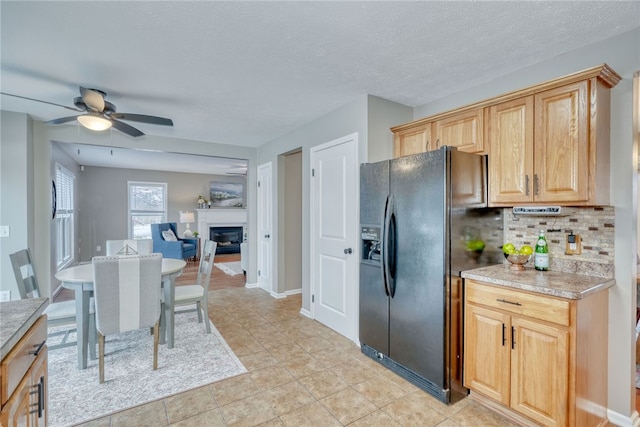 kitchen featuring a ceiling fan, light countertops, decorative backsplash, black refrigerator with ice dispenser, and a glass covered fireplace