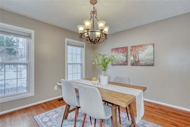 dining space featuring visible vents, baseboards, a chandelier, and wood finished floors