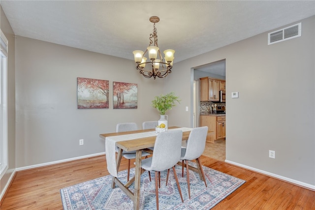 dining space with baseboards, visible vents, a notable chandelier, and light wood finished floors