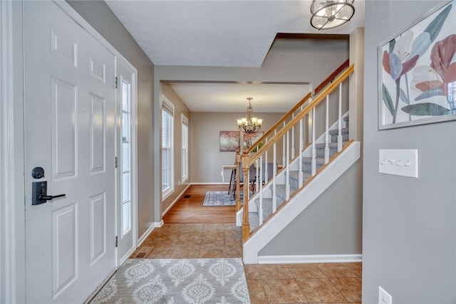 tiled entrance foyer featuring stairs, a chandelier, and baseboards