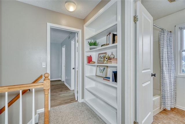 hallway featuring visible vents, baseboards, a textured ceiling, and an upstairs landing