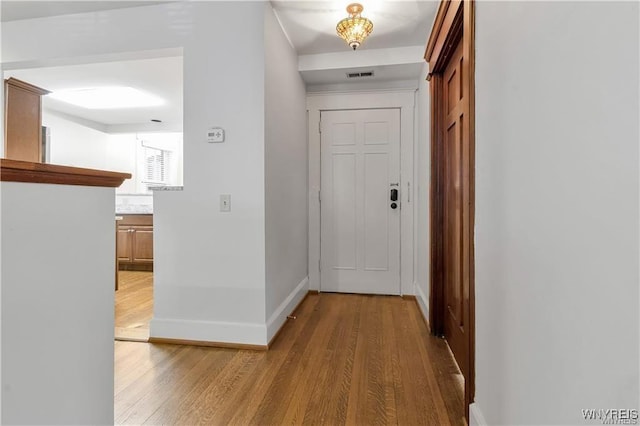 hall featuring light wood finished floors, visible vents, and baseboards