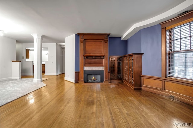 unfurnished living room with a large fireplace, decorative columns, baseboards, and wood finished floors