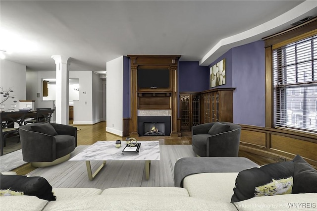 living area with a large fireplace, wood finished floors, and ornate columns