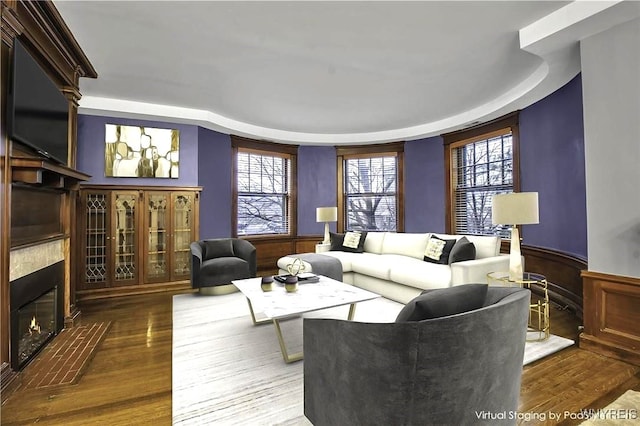 living area with a glass covered fireplace, wainscoting, and wood finished floors