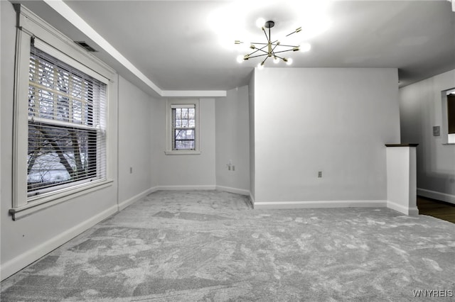 carpeted spare room with a chandelier, visible vents, and baseboards