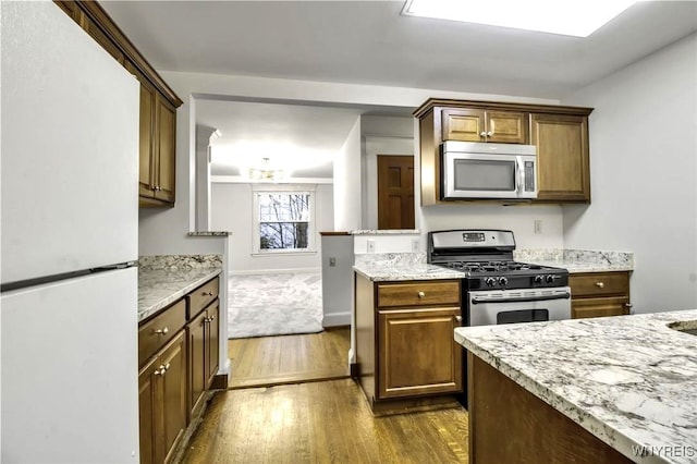 kitchen featuring baseboards, brown cabinetry, light stone counters, dark wood-style flooring, and stainless steel appliances