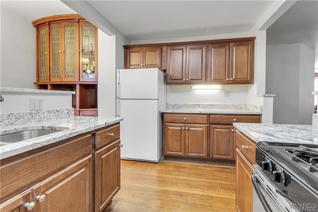 kitchen featuring light stone counters, glass insert cabinets, light wood-style flooring, freestanding refrigerator, and gas range