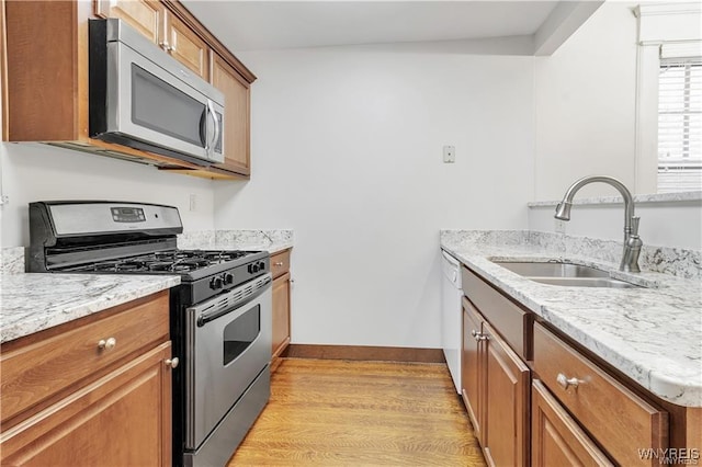 kitchen with appliances with stainless steel finishes, brown cabinets, a sink, and light wood-style flooring