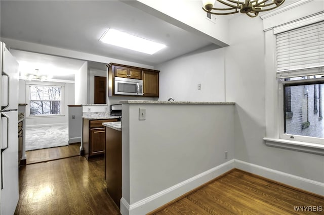 kitchen featuring dark wood finished floors, a notable chandelier, stainless steel microwave, freestanding refrigerator, and a peninsula